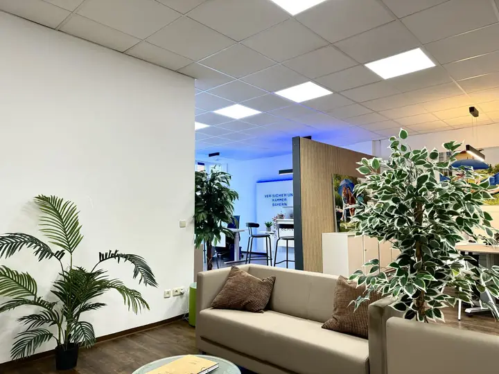Sitzecke mit Sofa und Pflanzen, dahinter die Arbeitsplätze