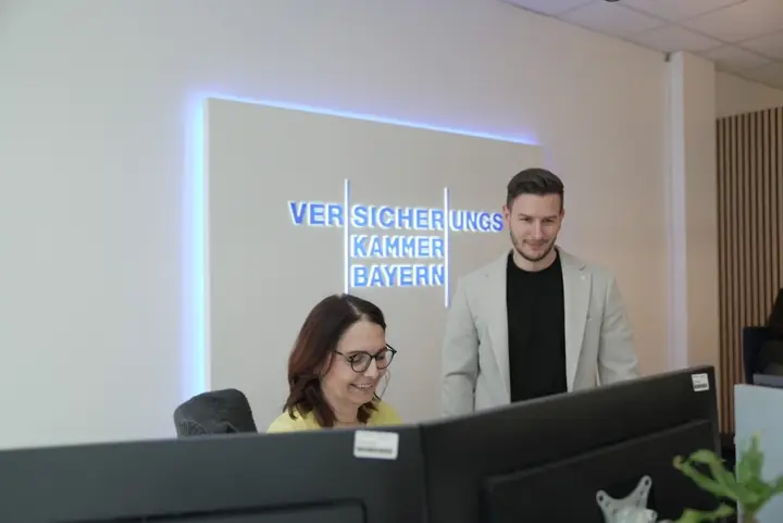 Maria Engelhardt und Patrick Bito am Empfang vor dem Logo der Versicherungskammer Bayern